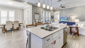 Una cocina moderna con una isla central, armarios blancos y un comedor con sillas.