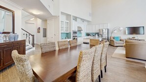 A spacious living area with a wooden dining table, wicker chairs, a sofa, and a TV. - Gulf-View Palmilla Resort Condo | Pool, On-Site Dining & Beach Boardwalk (Port Aransas)