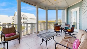 A covered balcony with a table and chairs, a sofa, and a view of neighboring houses. - Gulf-View Palmilla Resort Condo | Pool, On-Site Dining & Beach Boardwalk (Port Aransas)
