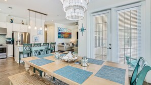 A spacious dining area with a wooden table, blue placemats, and a chandelier. - Shorely the Best | Palmilla Condo with Pool, Dining & Boardwalk to Beach (Port Aransas)