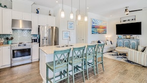 A modern kitchen with white cabinetry, stainless steel appliances, and a central island with bar stools. - Shorely the Best | Palmilla Condo with Pool, Dining & Boardwalk to Beach (Port Aransas)