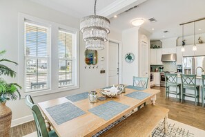 Enjoy dining in style with a large table set for four, surrounded by a modern chandelier and a view of the adjacent kitchen.