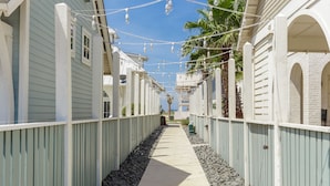 Un sendero estrecho bordeado por edificios azul claro con detalles blancos, que conduce a una zona cubierta con una palmera.