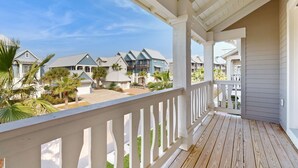 Una terraza de madera con barandilla blanca que da vista a una zona residencial con casas y palmeras.