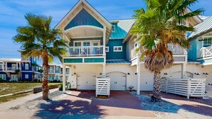 A large, multi-story house with a prominent balcony, a garage, and a well-maintained driveway. - Perfect Palmilla Beach Townhome | Near Resort Pool, Beach Access & Golf (Port Aransas)