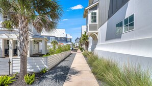 A residential street with modern houses, a palm tree, and a concrete pathway. - Perfect Palmilla Beach Townhome | Near Resort Pool, Beach Access & Golf (Port Aransas)