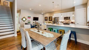 A modern kitchen with white cabinets, a microwave, and a refrigerator. There is a dining area with a wooden table and wicker chairs. - Upscale townhouse near the pool with bikes, resort boardwalk & golf course (Port Aransas)