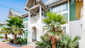 A multi-story building with a white exterior and green accents, featuring balconies and a covered entrance. - Upscale townhouse near the pool with bikes, resort boardwalk & golf course (Port Aransas)