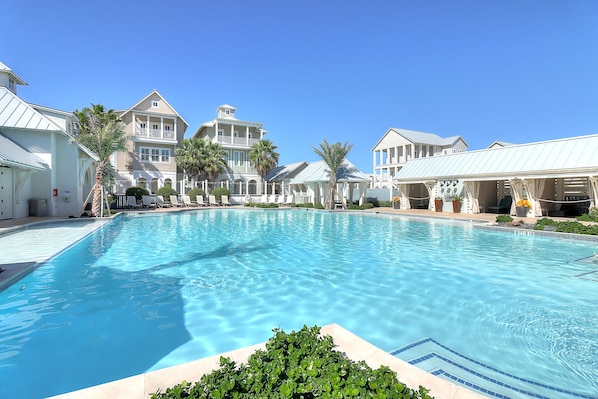 A large swimming pool surrounded by multi-story buildings with balconies and palm trees.