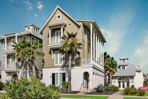 Stylish residential building with a central entrance and balconies on each floor, surrounded by lush tropical plants.