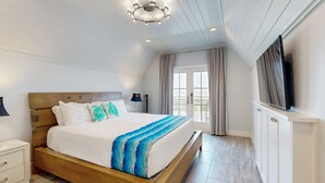 Un dormitorio con una cama de madera, paredes blancas, una lámpara en el techo, un televisor y una ventana con cortinas.