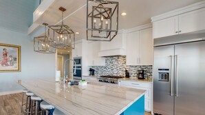 Una cocina moderna con una isla grande, electrodomésticos de acero inoxidable y una lámpara colgante de diseño geométrico.