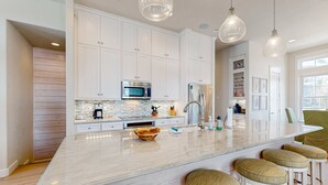 Una cocina moderna con muebles blancos, una isla grande con taburetes, electrodomésticos de acero inoxidable e iluminación colgante.