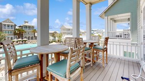 Terraza de madera con mobiliario exterior, con vistas a una piscina y una propiedad frente a la playa.