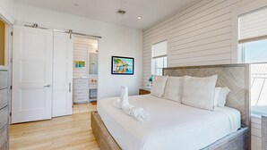 A bedroom with a large bed, a wooden headboard, a white door, and a view of the outside through a window.