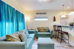 Relax in this stylish living room with a sofa, ottoman, and kitchen area, offering a view of the outside through the window.