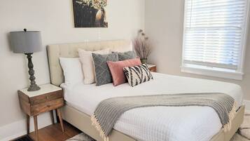 A bedroom with a bed, bedside table, lamp, and a painting on the wall.