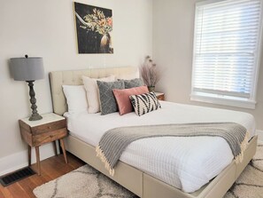 A bedroom with a bed, bedside table, lamp, and a painting on the wall. - Downtown Main Street One-Bedroom Suite w/ Hi-Speed Wifi (Shelbyville)