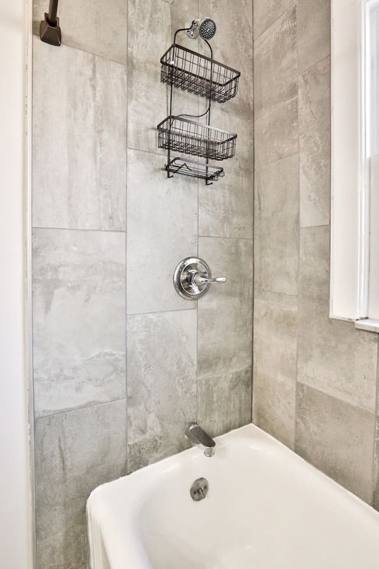 A bathroom with a white bathtub, a shower with a handheld showerhead, and a metal towel rack.