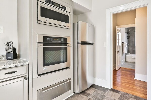 A kitchen with a stainless steel refrigerator, a microwave, and an oven. There is a countertop with a knife block.