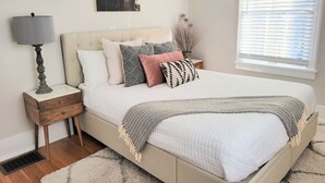 A bedroom with a bed, bedside table, lamp, and a painting on the wall. - Downtown Main Street One-Bedroom Suite w/ Hi-Speed Wifi (Shelbyville)