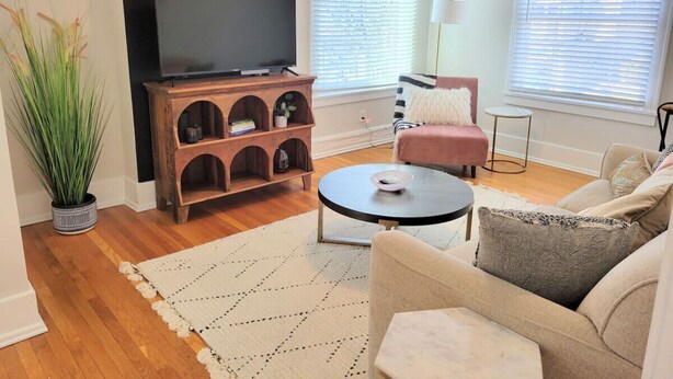 A living room with a TV, a wooden entertainment unit, a round coffee table, and a sofa. - Downtown Main Street One-Bedroom Suite w/ Hi-Speed Wifi (Shelbyville)