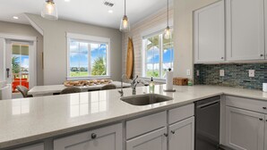 A modern kitchen with a large island, white cabinetry, and a view of the outdoors. - Palmilla Beach | Sunset-View End Unit | Garage & All-Suite | Steps to Pool (Port Aransas)
