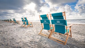 Beach chairs lined up on a sandy beach with a logo on the backrest. - Palmilla Beach | Sunset-View End Unit | Garage & All-Suite | Steps to Pool (Port Aransas)