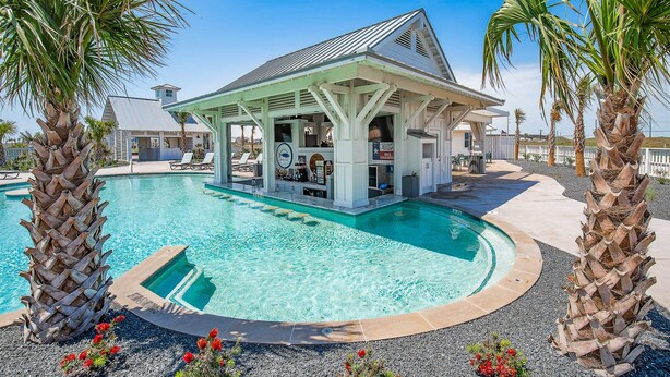 A pool area with a covered bar and lounge, surrounded by palm trees and a clear blue sky. - Palmilla Beach | Sunset-View End Unit | Garage & All-Suite | Steps to Pool (Port Aransas)