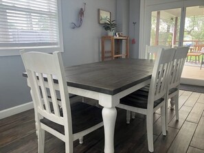 A dining area with a wooden table and white chairs, a window with blinds, and a view of a deck.