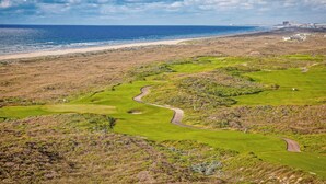 A coastal golf course with a view of the ocean and a distant city skyline. - Luxe Townhome in Palmilla Beach Resort | Beach Service, Pool & Golf Course (Port Aransas)