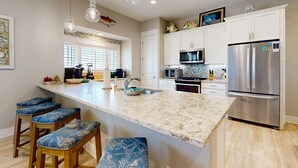 A modern kitchen with a large island, bar stools, stainless steel appliances, and decorative fish on the cabinets. - Luxe Townhome in Palmilla Beach Resort | Beach Service, Pool & Golf Course (Port Aransas)
