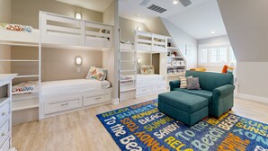 Un dormitorio con literas, un sillón verde azulado y una alfombra con motivos playeros.