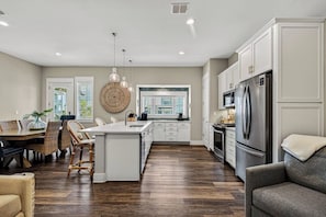 A modern kitchen with white cabinetry, a central island, and a dining area with wicker chairs.