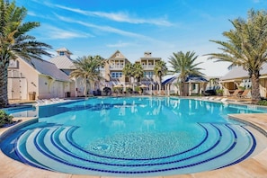 A swimming pool with lounge chairs, palm trees, and a building with a triangular roof.