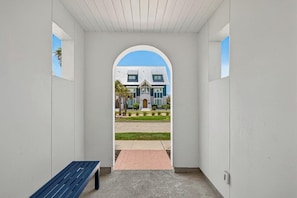 A corridor with a bench, leading to a building with a large arched entrance.
