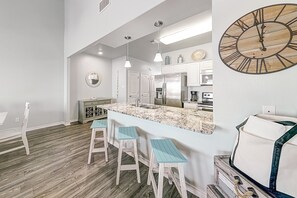 A modern kitchen with a central island, bar stools, and a large wall clock.