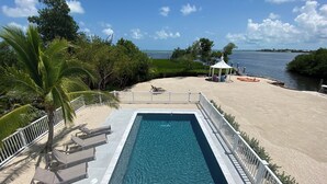 A swimming pool with a white deck, surrounded by a sandy beach and a gazebo. - Latitudes - Ocean front with salt water pool. (Cudjoe Key)