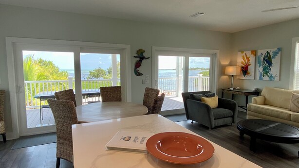 A spacious living area with a large table, comfortable seating, and a view of the ocean. - Latitudes - Ocean front with salt water pool. (Cudjoe Key)
