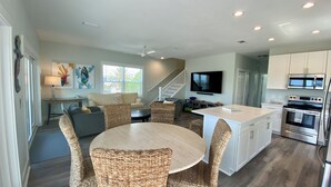 A modern kitchen with stainless steel appliances, a dining area with wicker chairs, and a living space with a sofa and artwork. - Latitudes - Ocean front with salt water pool. (Cudjoe Key)