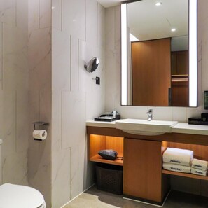 Ein modernes Badezimmer mit Marmorwand, einem großen Spiegel, einem Waschbecken und einer Toilette.