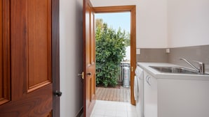 A narrow kitchen with a wooden door, a white sink, and a view of a green bush outside. - Telegraph Station (Gulgong)