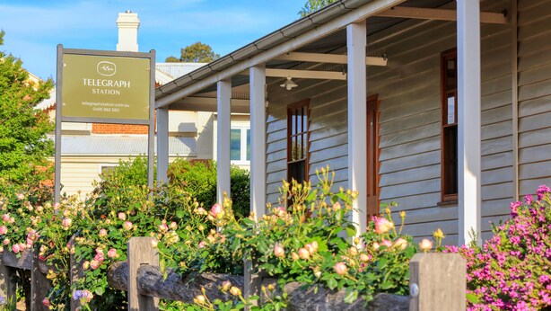 A traditional building with a sign for a Telegraph Station, surrounded by flowering plants and a wooden fence. - Telegraph Station (Gulgong)