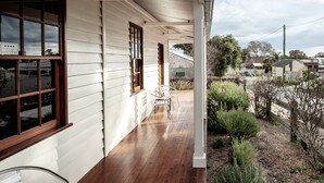 A covered porch with wooden flooring, a white exterior wall, and a window with a sign. - Telegraph Station (Gulgong)
