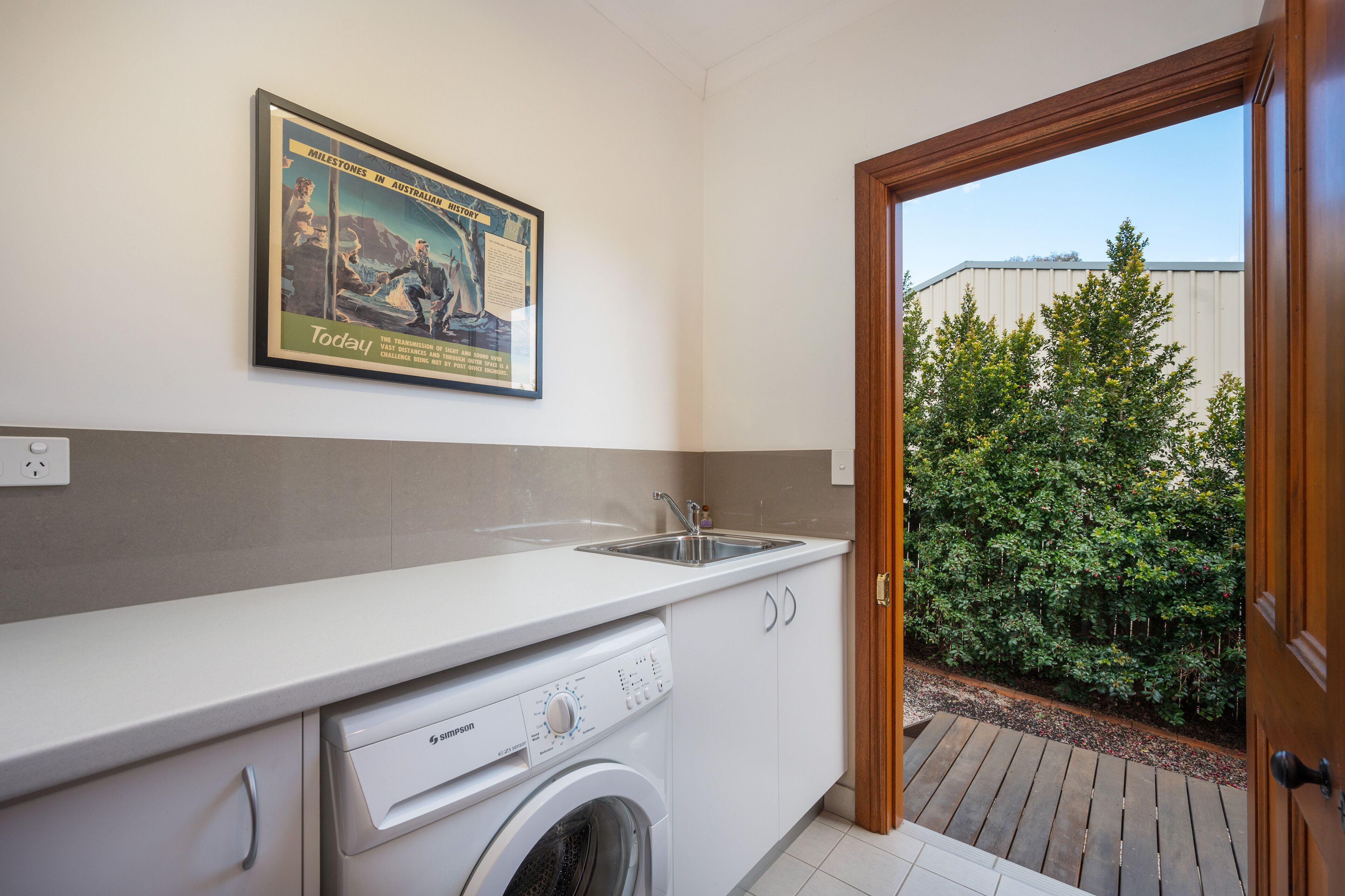 Cocina compacta con lavadora, un lavabo y un cartel histórico enmarcado.
