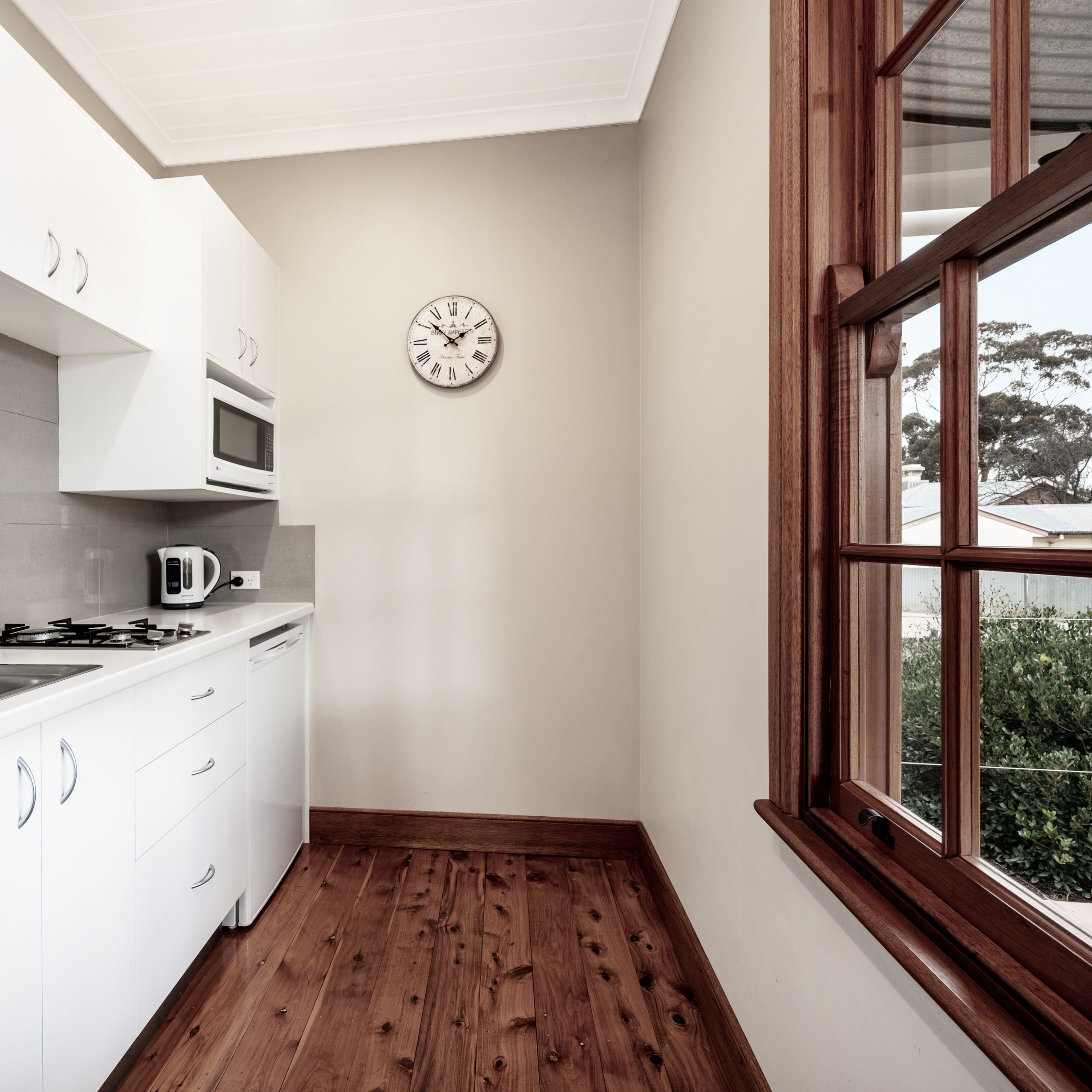 A kitchen with white cabinets, a microwave, a kettle, and a wooden floor.