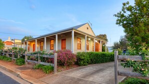 A two-story house with a porch, surrounded by a wooden fence and flowering plants. - Telegraph Station (Gulgong)