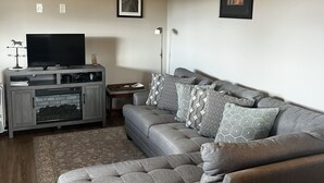 A living room with a grey sofa, a television, and a ceiling fan. - River Rest Luxury Cabin - The Big Hole. Beautiful River and Mountain Views!! (Silver Star)