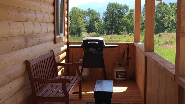 A wooden deck with a bench and a grill, overlooking a grassy area with trees. - River Rest Luxury Cabin - The Big Hole. Beautiful River and Mountain Views!! (Silver Star)