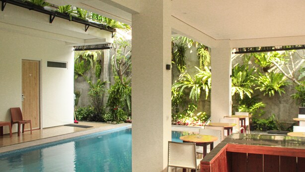 A pool area with a long pool, seating, and lush greenery.